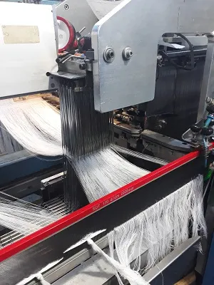 Otomatik tahar makinesinde gücülerden geçirilen beyaz çözgü iplikleri